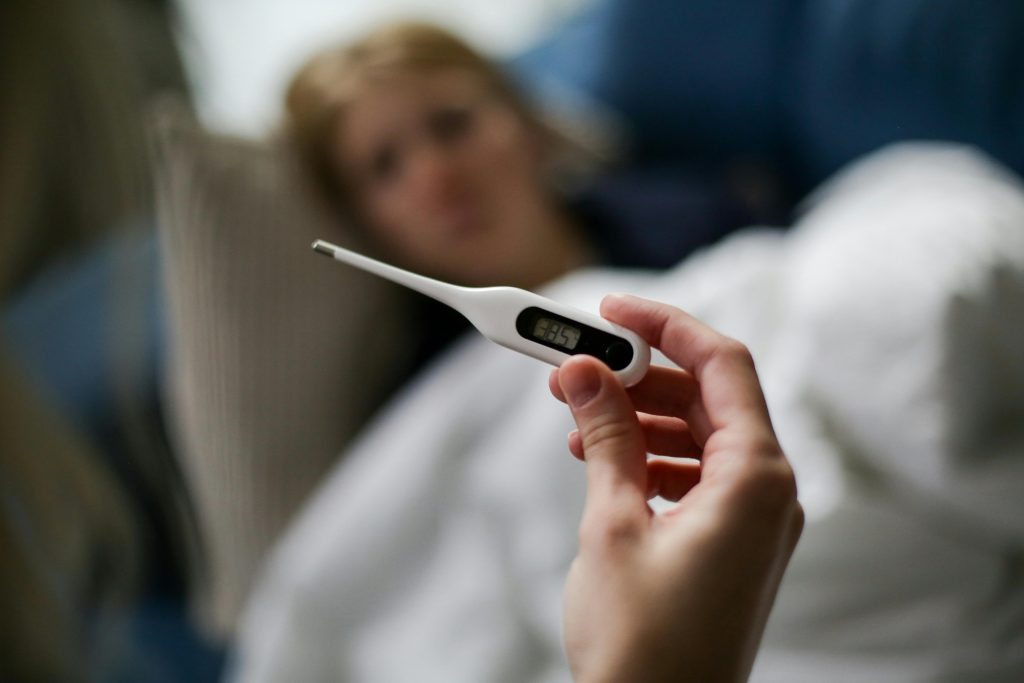 Person holding a thermometer with a sick person in the background