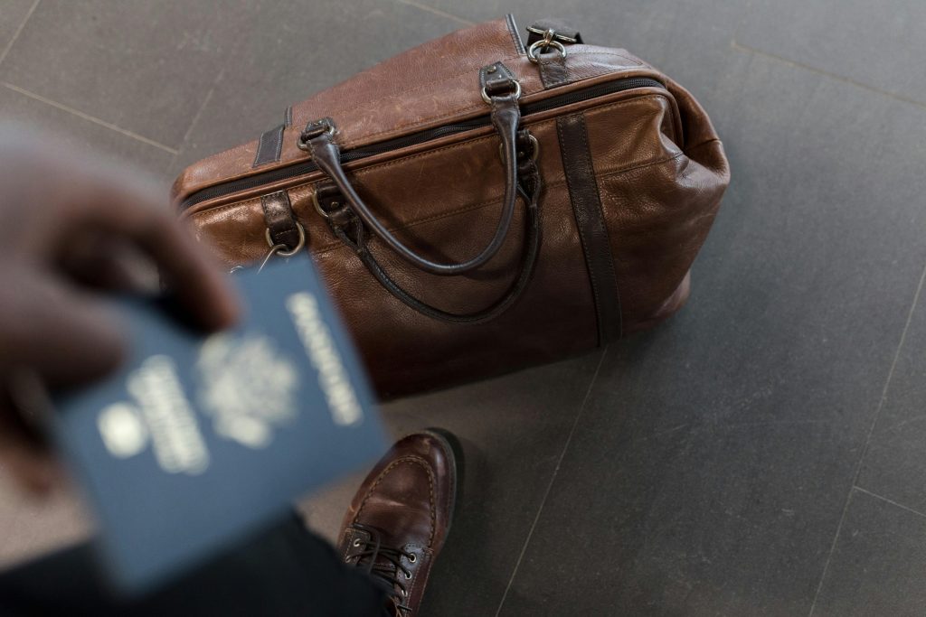 Image of a person holding their passport with their luggage on the ground